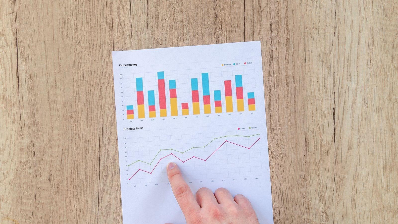 Ahşap masadaki basılı grafik çıktısında bir noktayı parmağıyla gösteren el